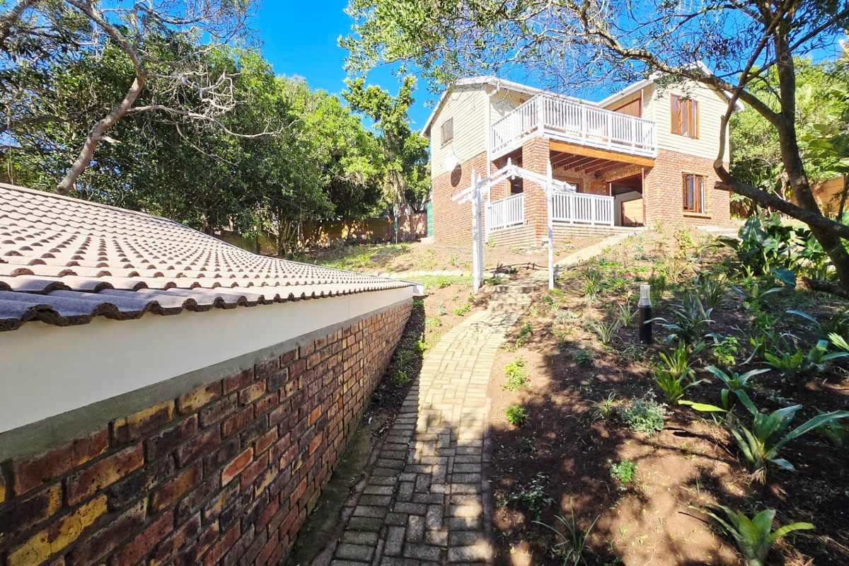 Rear view of the property featuring a brick boundary wall, paved garden path, and a two-story structure with a balcony.