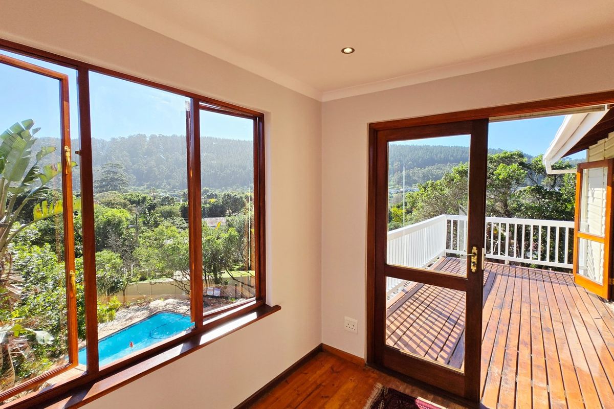Bright living area featuring polished timber floors, large windows with scenic views, and direct access to an expansive outdoor timber deck.