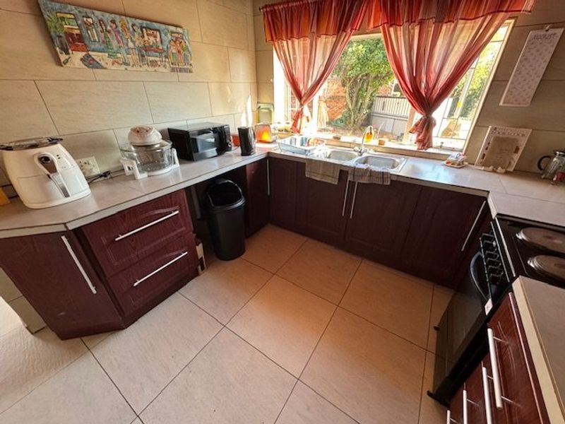 A functional kitchen featuring dark wood-look cabinetry, tiled splashbacks, tiled flooring, and a double basin sink overlooking the garden.