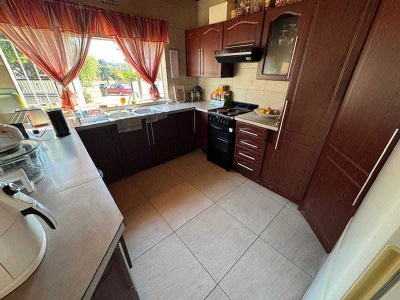 A functional kitchen featuring dark wood-look cabinetry, tiled flooring, a double basin sink, and a built-in extractor fan with a freestanding stove.