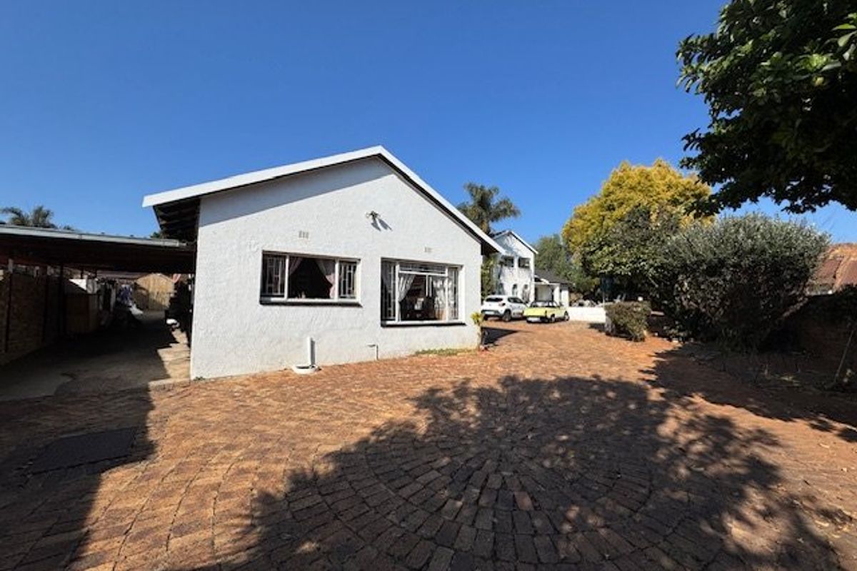 Rear view of the property featuring a paved driveway, carport, and white exterior walls with security bars on the windows.
