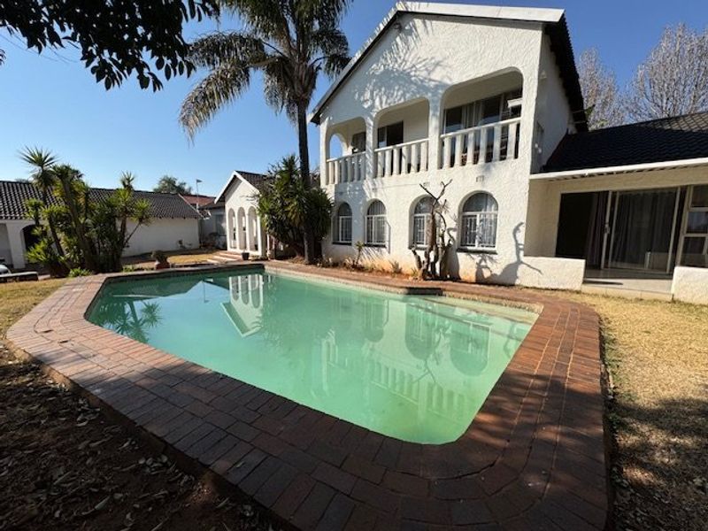 Rear exterior view featuring a swimming pool with brick coping, set against a multi-story home with arched balconies and a tiled roof.