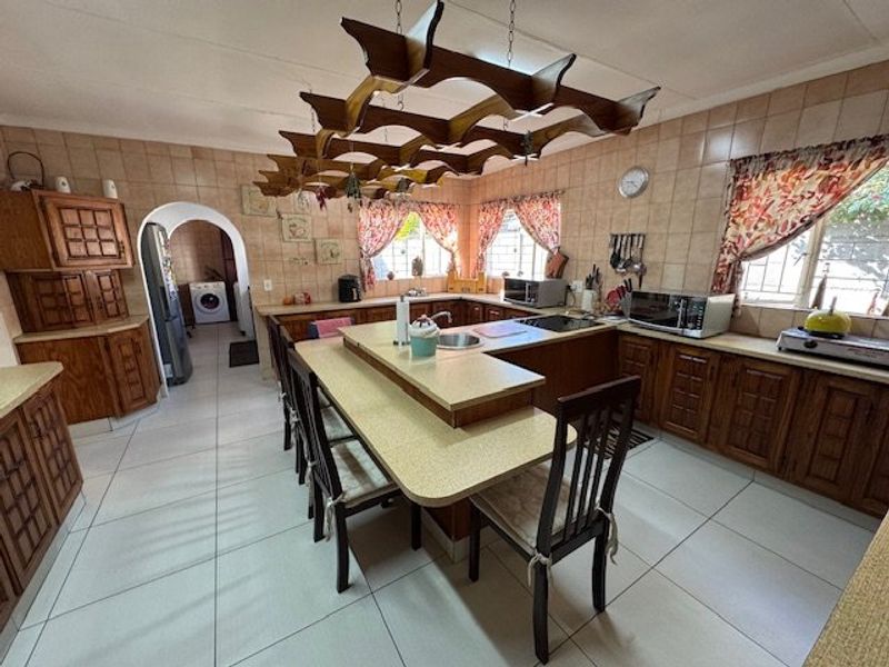 Spacious kitchen featuring extensive wooden cabinetry, laminate countertops, a central breakfast bar, and a distinctive decorative wooden ceiling structure.