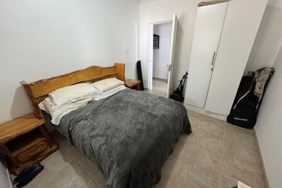 A functional bedroom featuring tiled flooring, a built-in wardrobe, and neutral wall finishes, offering a clean and practical living space.