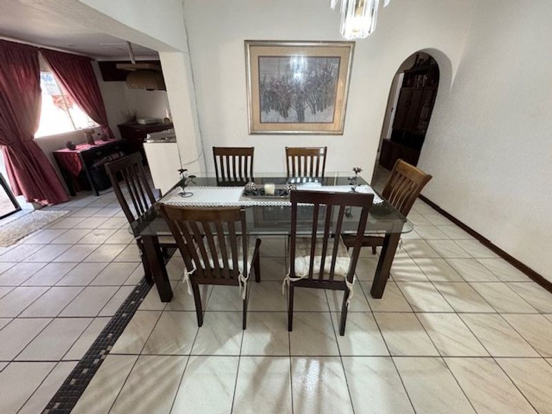 A dining area featuring ceramic tile flooring, an arched doorway leading to adjacent spaces, and a central pendant light fixture.