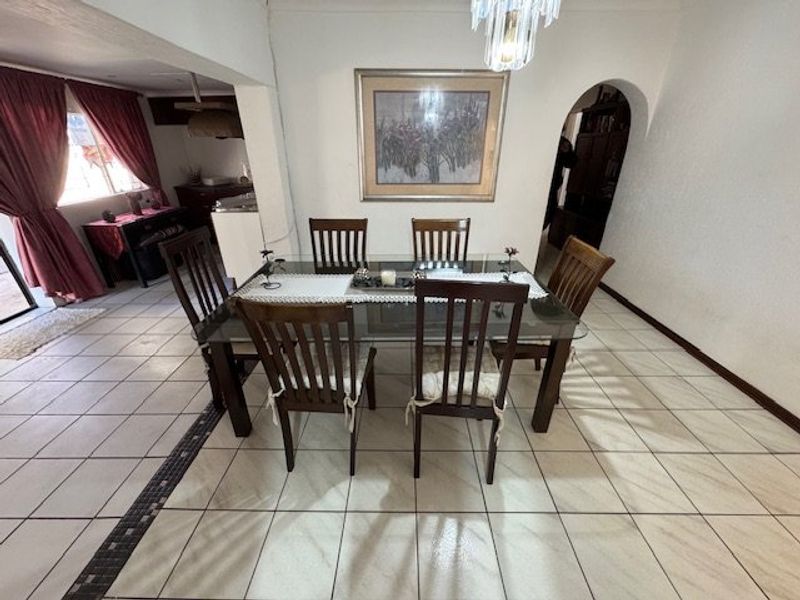 A dining area featuring ceramic floor tiles, an arched doorway, and a central pendant light fixture, providing a functional space for meals.