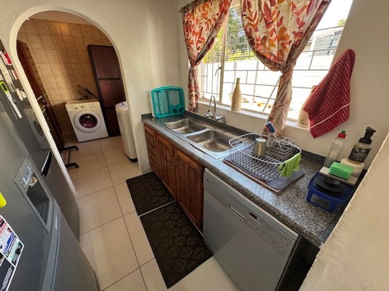 Functional scullery area featuring double bowl sink, granite countertops, and wooden cabinetry, with an adjacent laundry space visible through the arched doorway.