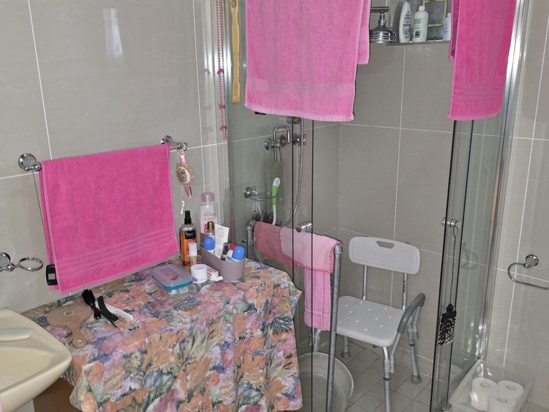 A functional bathroom featuring a glass-enclosed shower, ceramic basin, and toilet with neutral wall tiling throughout.