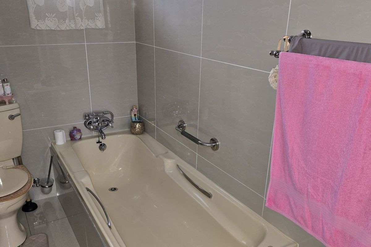 A functional bathroom featuring tiled walls and floors, a standard bathtub with a grab bar, and a toilet.