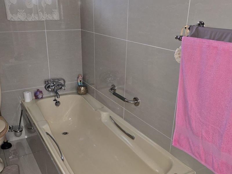 A functional bathroom featuring tiled walls and floors, a standard bathtub with a grab bar, and a toilet.