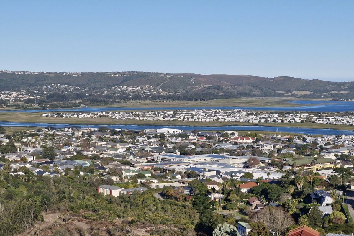 An elevated aerial view overlooking a residential coastal town, featuring expansive landscape vistas, water bodies, and surrounding hills.