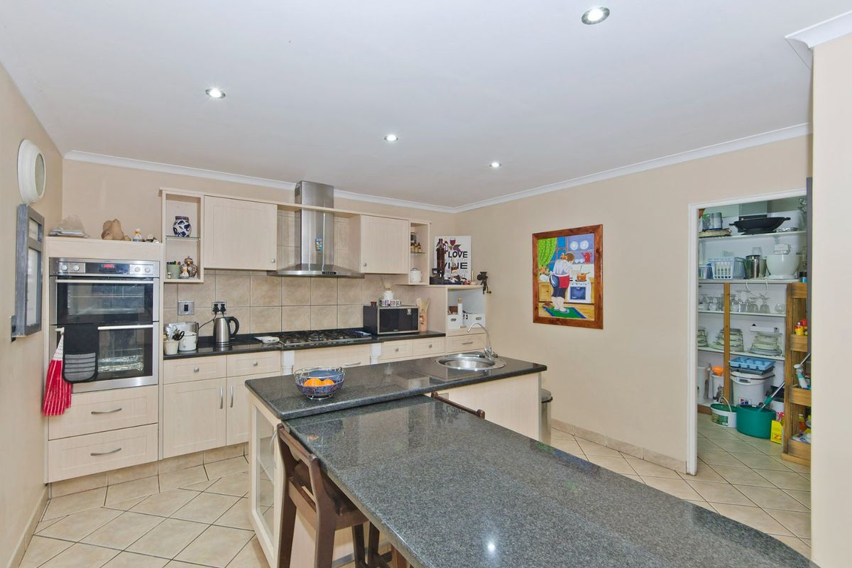A functional kitchen featuring granite countertops, built-in oven, gas hob, and an adjoining scullery area with tiled flooring and recessed lighting.