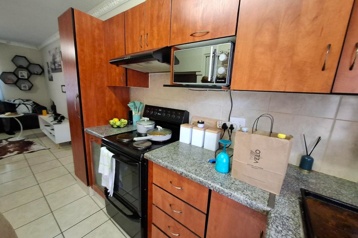 A functional kitchen featuring wood-finish cabinetry, granite countertops, and a built-in electric stove with an extractor fan, seamlessly flowing into the adjacent living area.