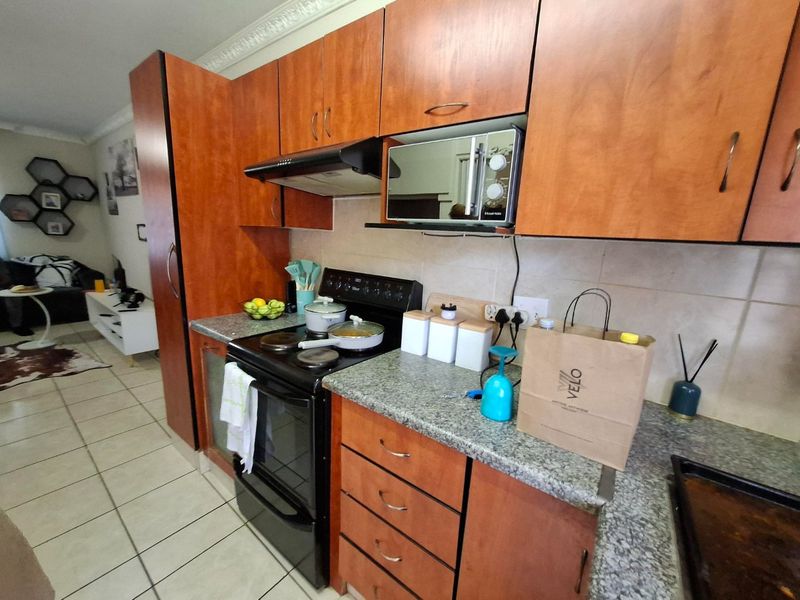 A functional kitchen featuring wood-finish cabinetry, granite countertops, and a built-in electric stove with an extractor fan, seamlessly flowing into the adjacent living area.