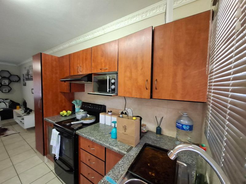 A functional kitchen featuring wood-finish cabinetry, granite-look laminate countertops, a built-in oven with extractor fan, and a stainless steel sink.