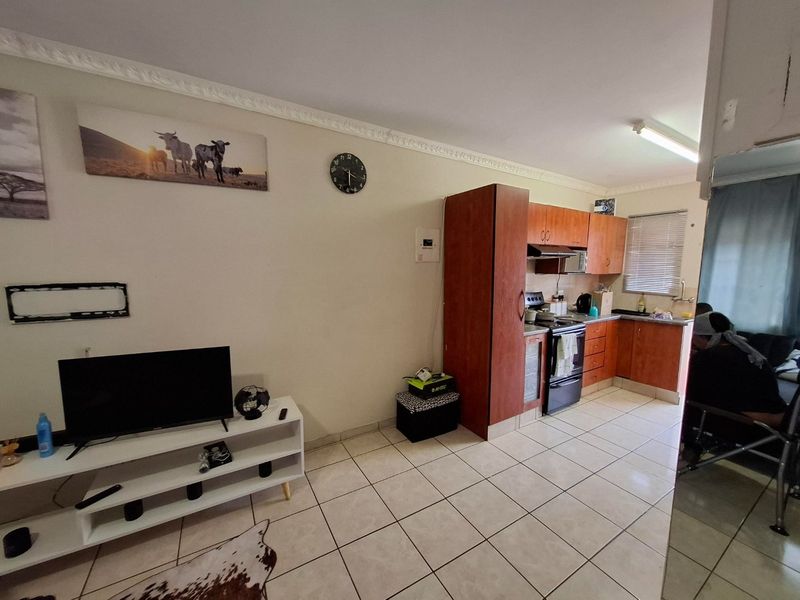 Open-plan living area featuring tiled flooring and a functional kitchen with built-in cabinetry, stove, and extractor fan.