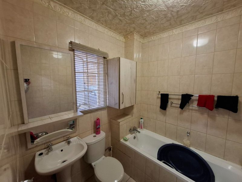 A functional bathroom featuring a pedestal basin, toilet, and bathtub with full-height wall tiling and decorative ceiling detailing.