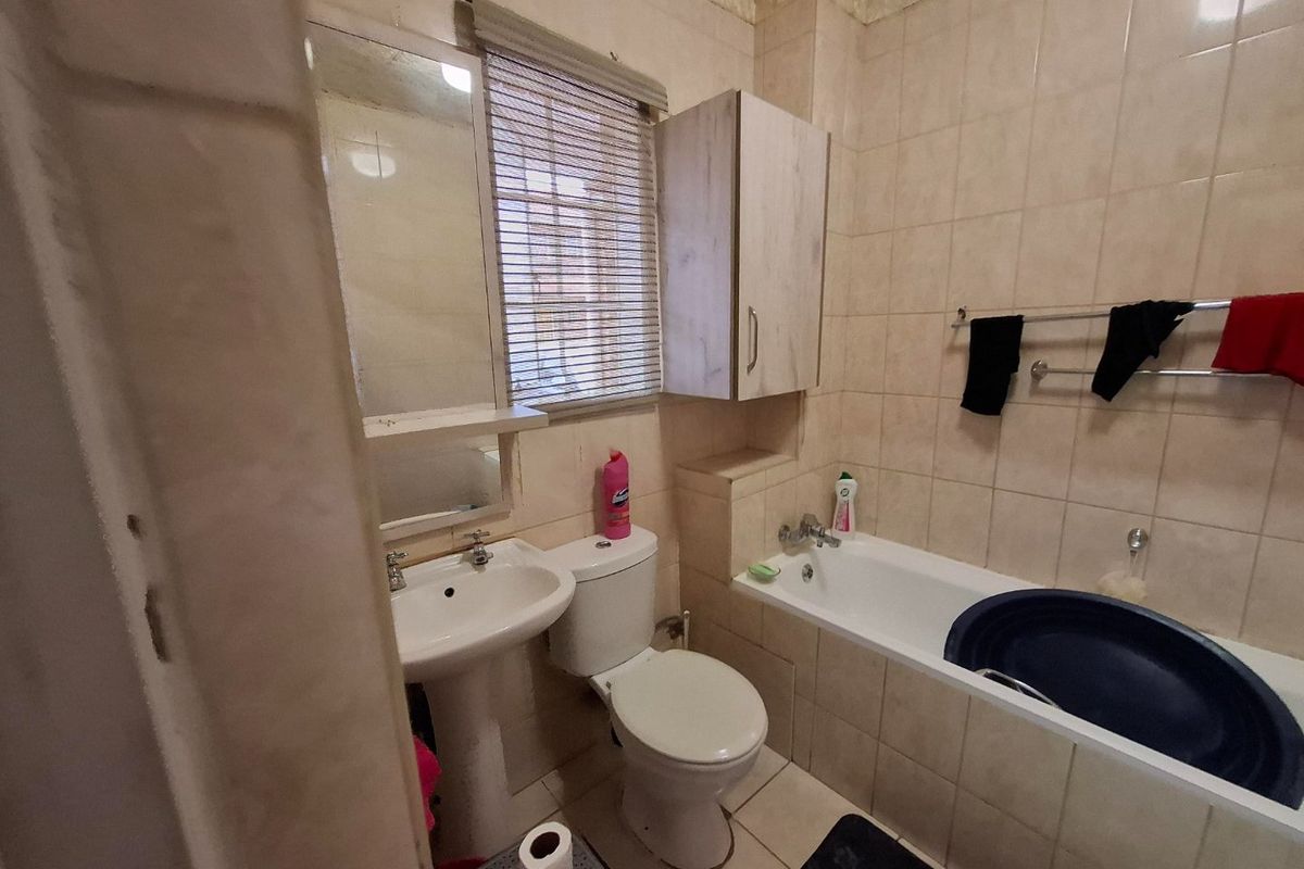 A compact bathroom featuring a pedestal basin, toilet, and bathtub with full-height wall tiling and a wall-mounted storage cabinet.