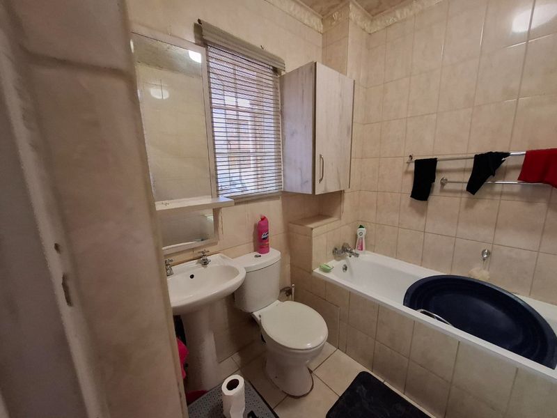 A compact bathroom featuring a pedestal basin, toilet, and bathtub with full-height wall tiling and a wall-mounted storage cabinet.