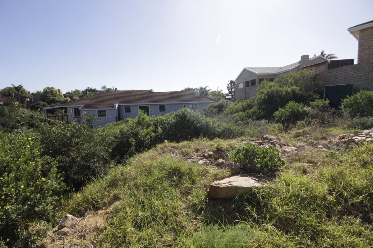 A view of the sloped, undeveloped residential land with surrounding established homes and natural vegetation in the background.