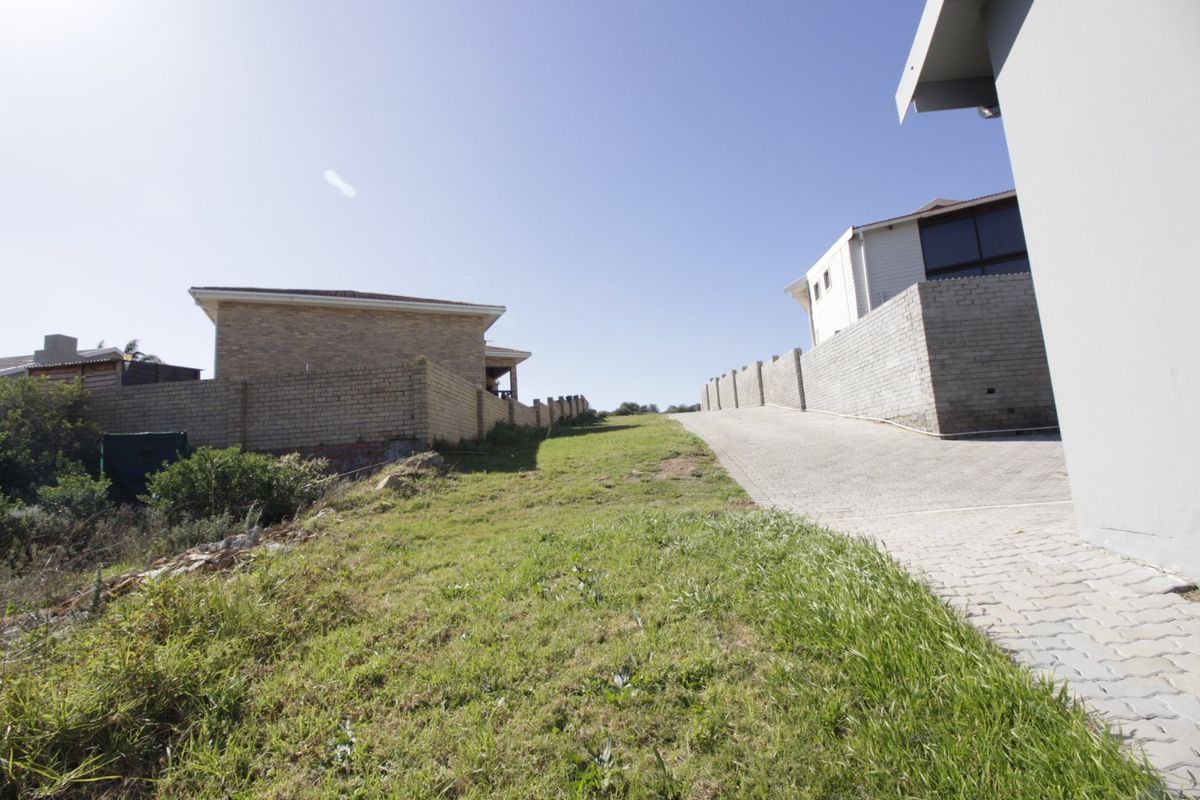 A view of a vacant residential plot featuring a paved driveway and established boundary walls, situated in a developed neighborhood.