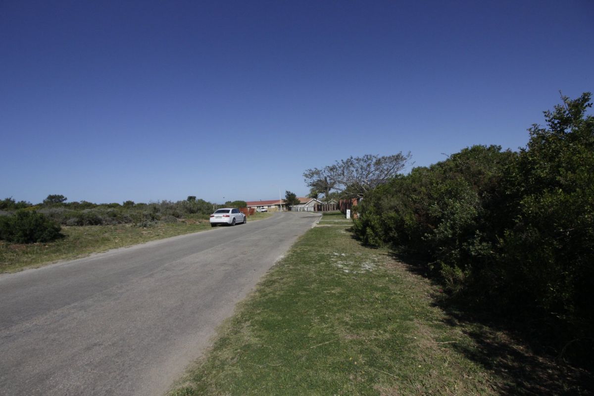 A view of the street approach and surrounding landscape, showing the paved road and natural vegetation bordering the residential area.