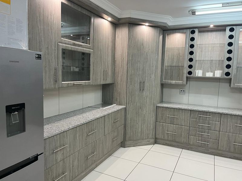 Modern kitchen featuring extensive wood-grain cabinetry, granite countertops, glass-fronted display units, and clean tiled flooring with integrated lighting.