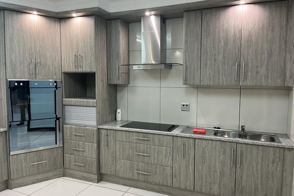 Modern kitchen featuring wood-grain laminate cabinetry, granite countertops, integrated oven, induction cooktop, stainless steel extractor fan, and double bowl sink.