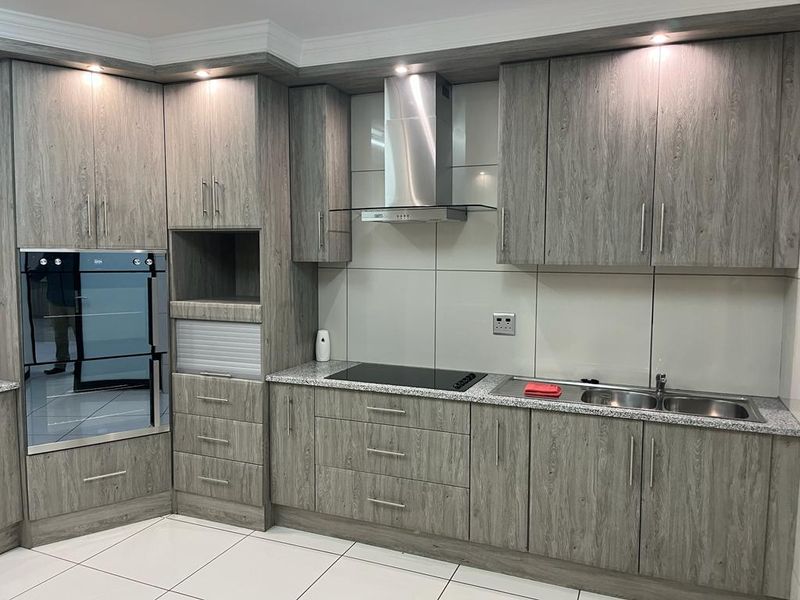 Modern kitchen featuring wood-grain laminate cabinetry, granite countertops, integrated oven, induction cooktop, stainless steel extractor fan, and double bowl sink.