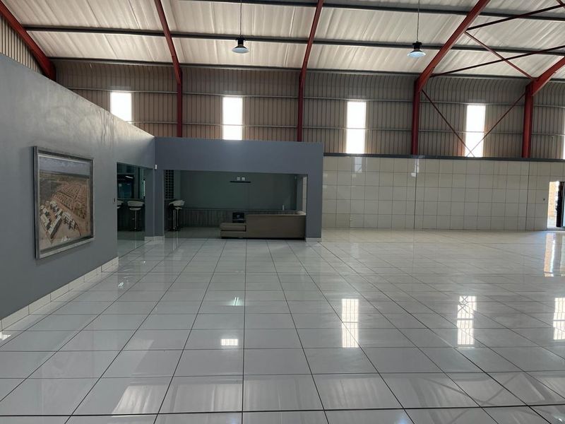 Spacious open-plan commercial area featuring high ceilings with exposed steel trusses, polished tiled flooring, and a built-in bar counter.