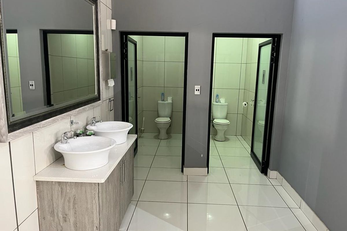 A clean, modern commercial bathroom featuring a dual vanity with vessel sinks, large wall mirror, and two separate toilet cubicles with tiled finishes.