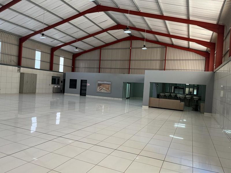 Spacious open-plan commercial warehouse area featuring high ceilings with exposed steel trusses, polished tiled flooring, and a built-in service counter.