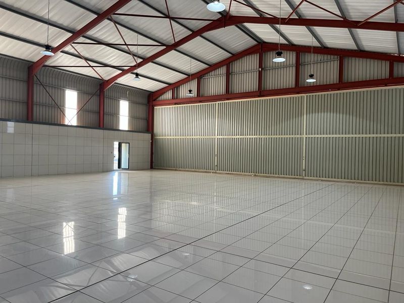 Spacious commercial warehouse or industrial unit featuring high ceilings with exposed steel trusses, polished tiled flooring, and large sliding access doors.