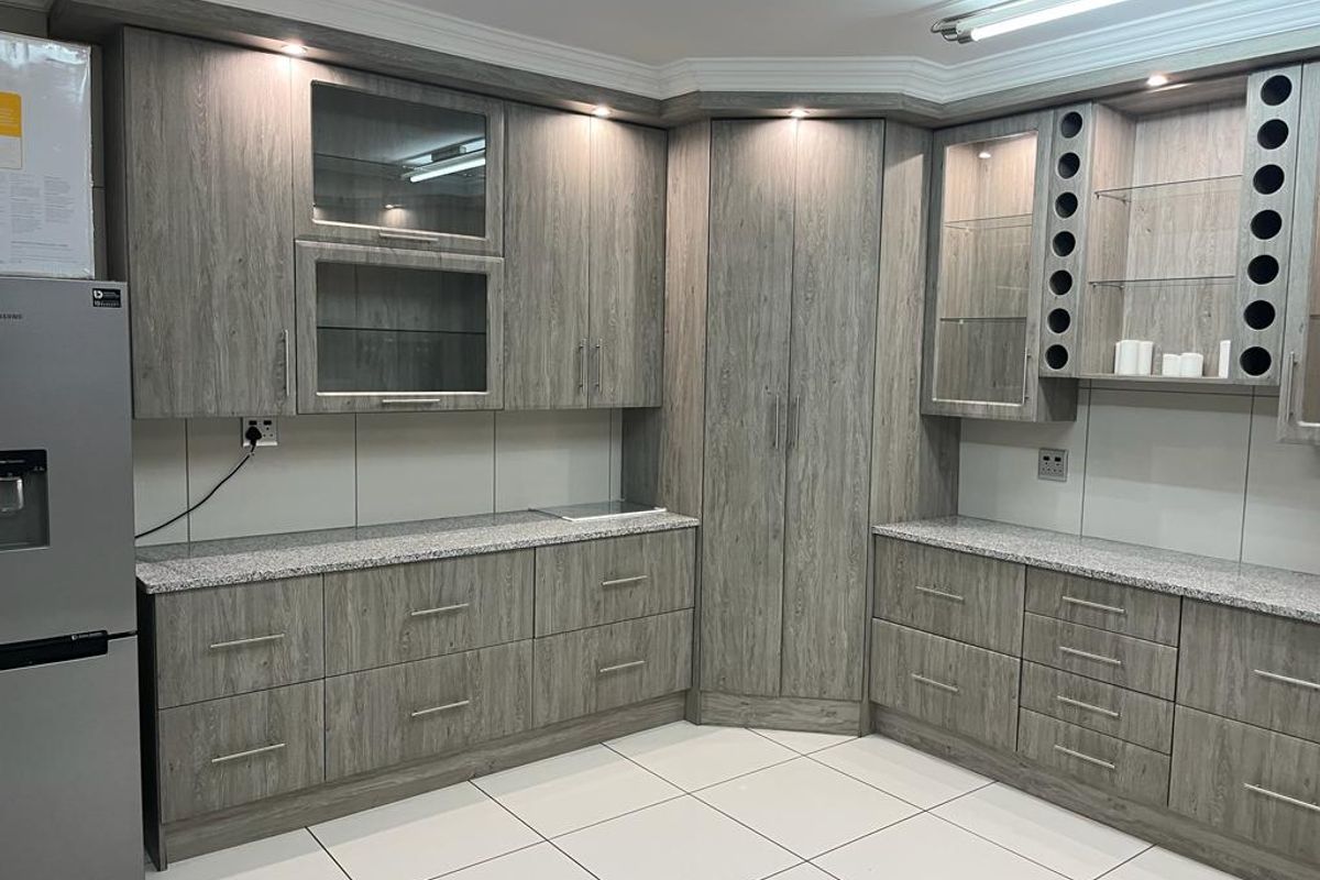 A modern kitchen featuring grey wood-grain cabinetry, granite countertops, integrated wine storage, and glass display shelving with recessed lighting.