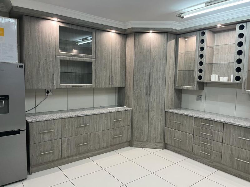 A modern kitchen featuring grey wood-grain cabinetry, granite countertops, integrated wine storage, and glass display shelving with recessed lighting.