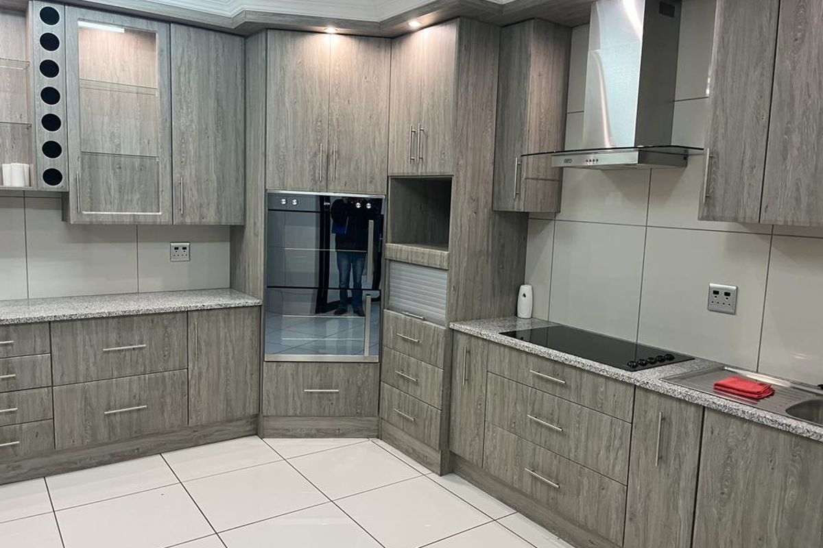 Modern kitchen featuring wood-grain cabinetry, granite countertops, integrated oven, electric hob, and stainless steel extractor fan with clean tiled flooring.