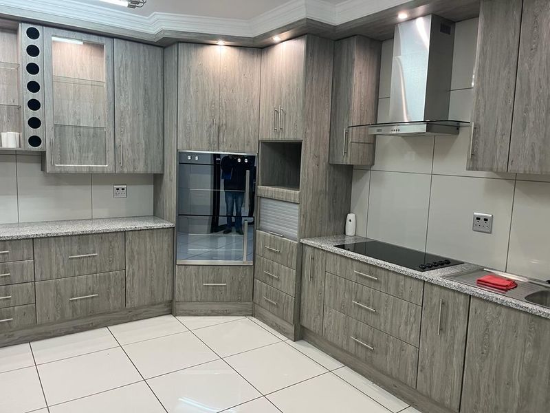 Modern kitchen featuring wood-grain cabinetry, granite countertops, integrated oven, electric hob, and stainless steel extractor fan with clean tiled flooring.