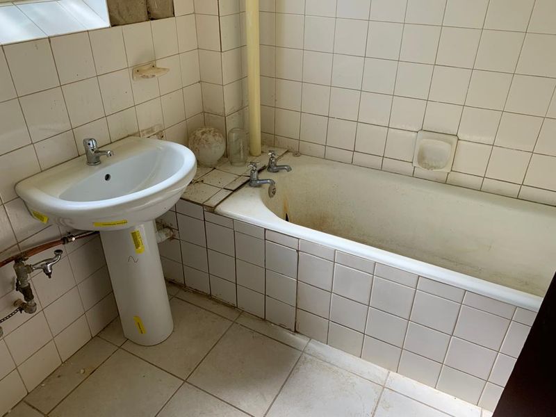 A dated bathroom featuring a pedestal basin and built-in bathtub with ceramic tiling, requiring significant renovation and modernization of fixtures and finishes.