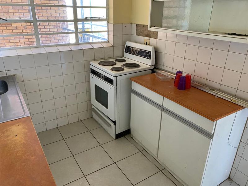 A dated kitchen featuring tiled splashbacks, white cabinetry, laminate countertops, and a freestanding stove, offering significant potential for modernization and renovation.