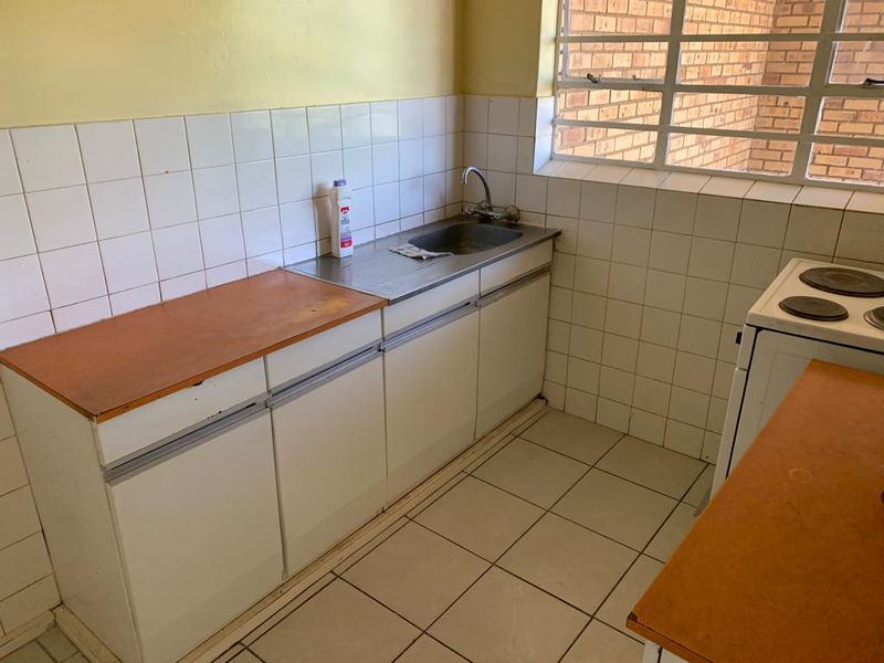A functional kitchen featuring tiled flooring, a stainless steel sink, and built-in cabinetry with a tiled backsplash, offering potential for modern renovation.