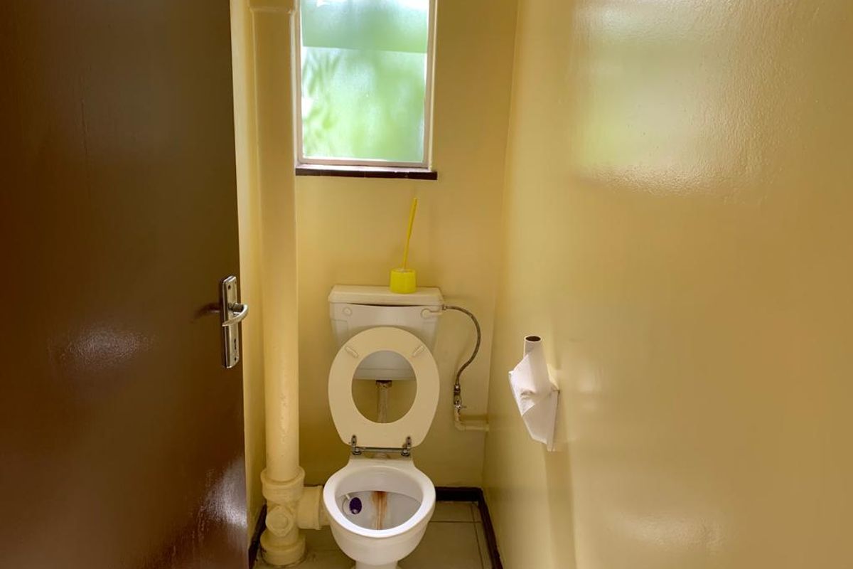 A compact bathroom featuring a standard toilet, tiled flooring, and an exposed vertical plumbing pipe, requiring cosmetic updates to improve its overall condition.