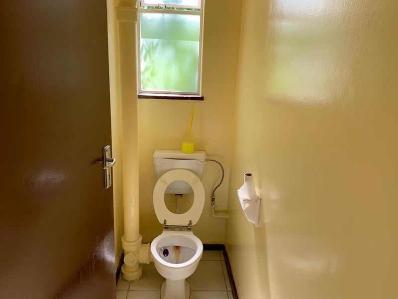 A compact bathroom featuring a standard toilet, tiled flooring, and an exposed vertical plumbing pipe, requiring cosmetic updates to improve its overall condition.