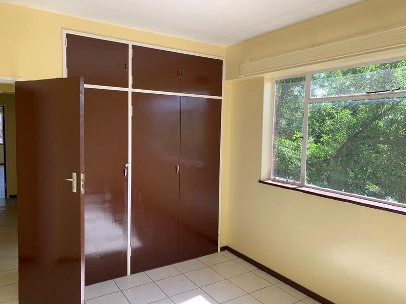 A bright, empty bedroom featuring tiled flooring, large windows with natural light, and built-in cupboards, offering a blank canvas for personalization.