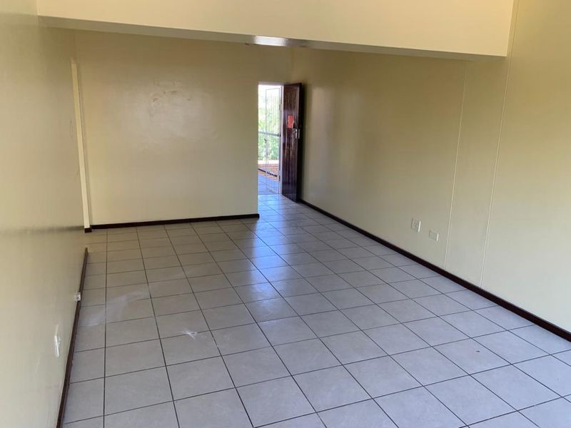 An empty, open-plan living area featuring neutral tiled flooring and access to an exterior balcony through a security gate.