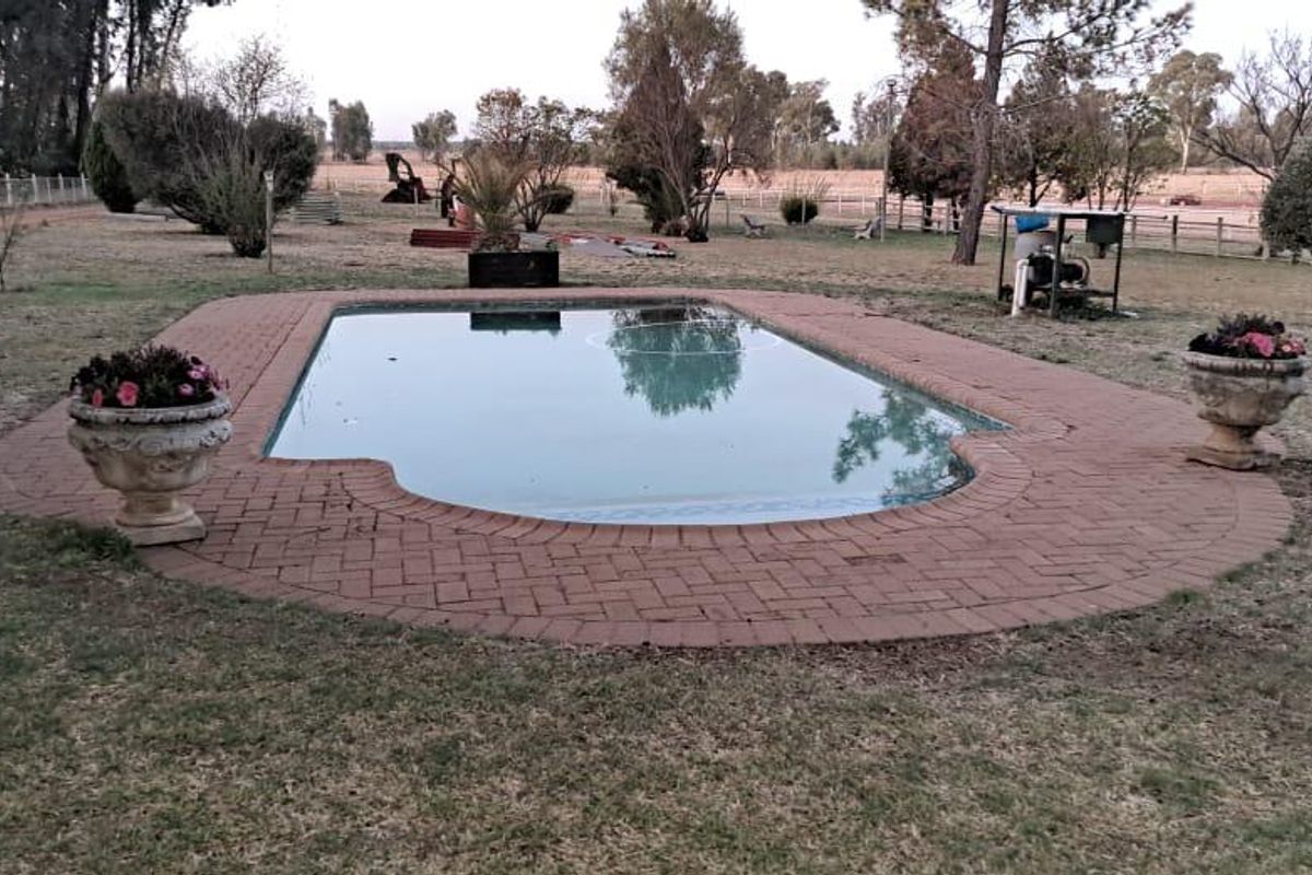 Outdoor swimming pool area featuring brick paving surround, set within a spacious farm garden landscape.
