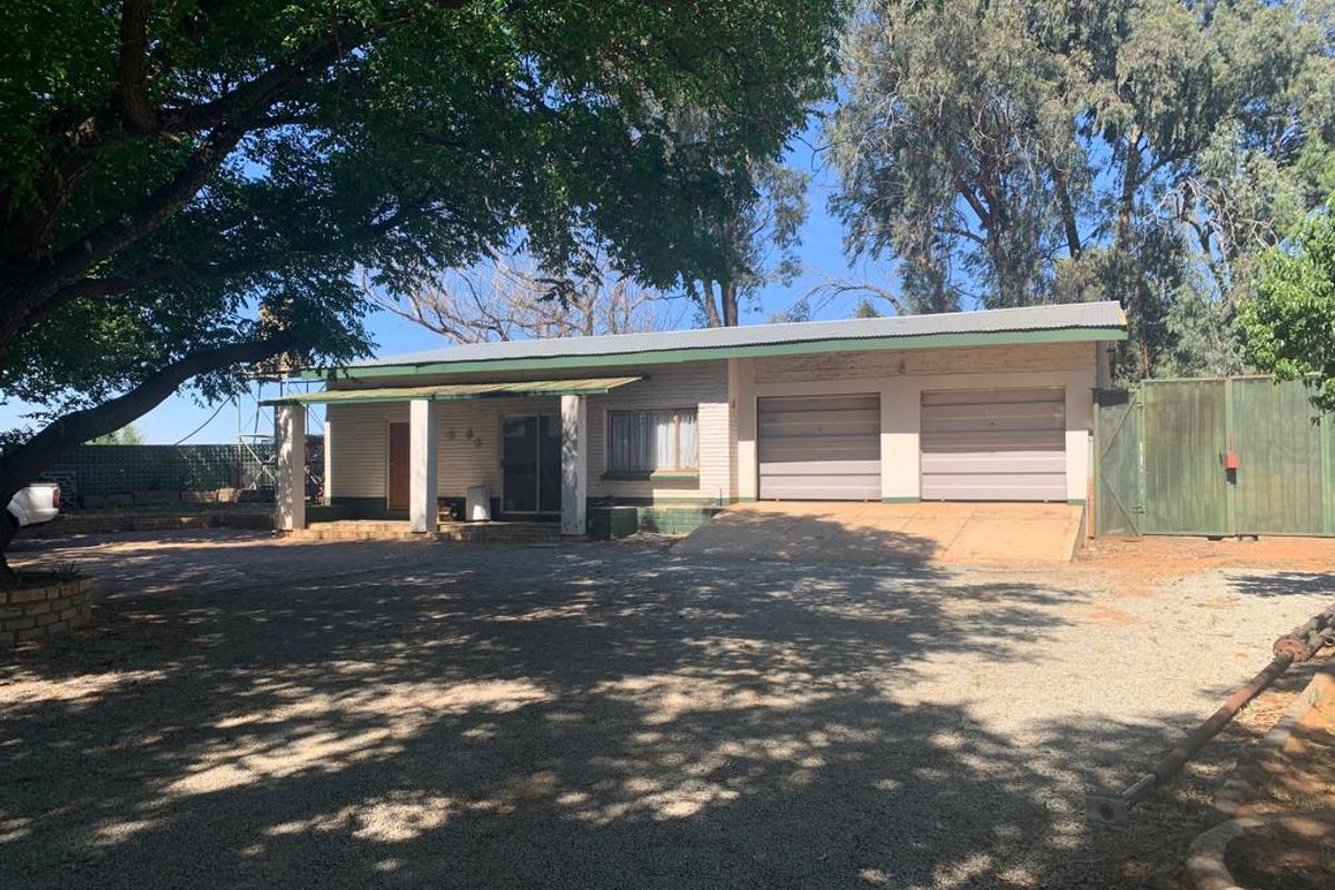 Front elevation of a farm-style residence featuring a double garage, covered entrance porch, and a gravel driveway set on a spacious rural property.