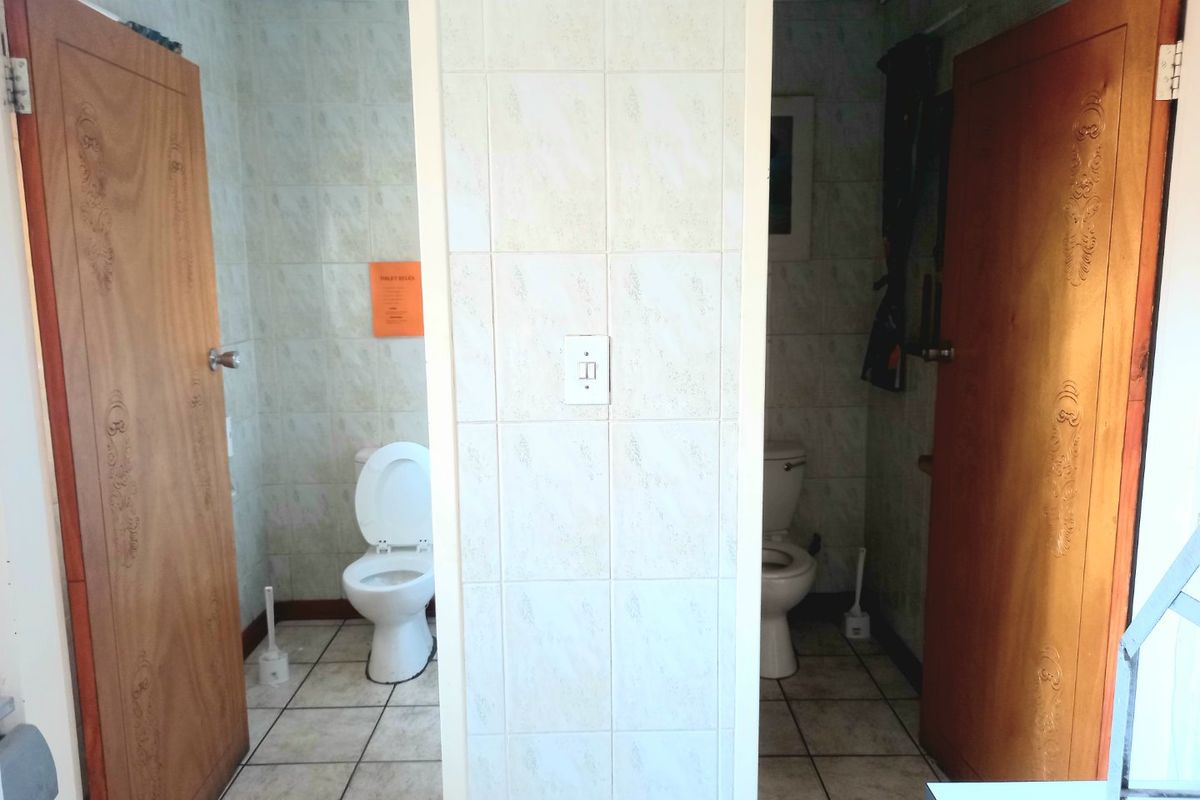 A commercial restroom facility featuring two separate toilet cubicles with tiled walls and floors, separated by a central tiled partition wall.