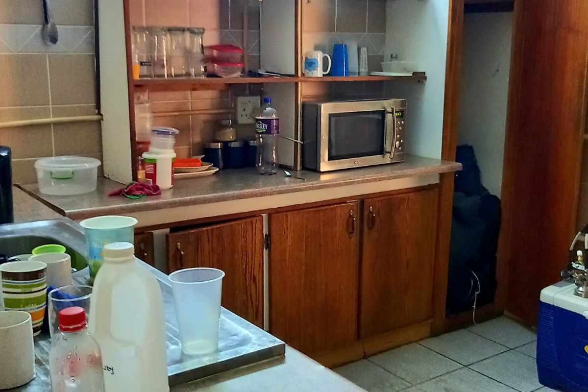 A dated kitchen area featuring laminate countertops, wooden cabinetry, and tiled wall splashbacks, requiring cosmetic updates to improve functionality and aesthetic appeal.