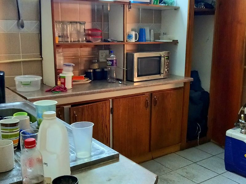 A dated kitchen area featuring laminate countertops, wooden cabinetry, and tiled wall splashbacks, requiring cosmetic updates to improve functionality and aesthetic appeal.