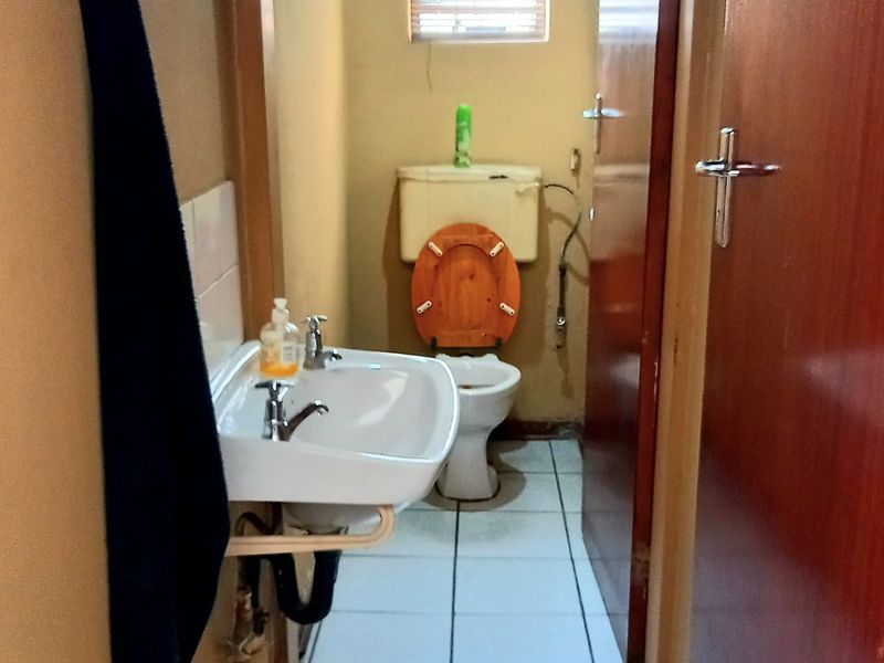 A functional bathroom featuring a wall-mounted basin, toilet, tiled flooring, and a window with a venetian blind.
